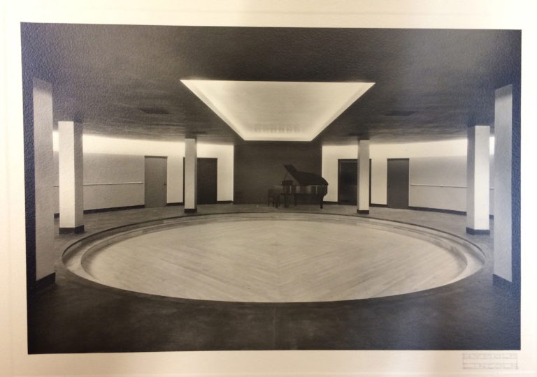 Black and white photo of a round dance studio with a baby grand piano. 
