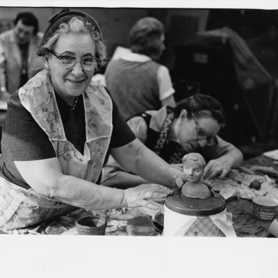 Black and white photo of an elderly woman sculpting clay.